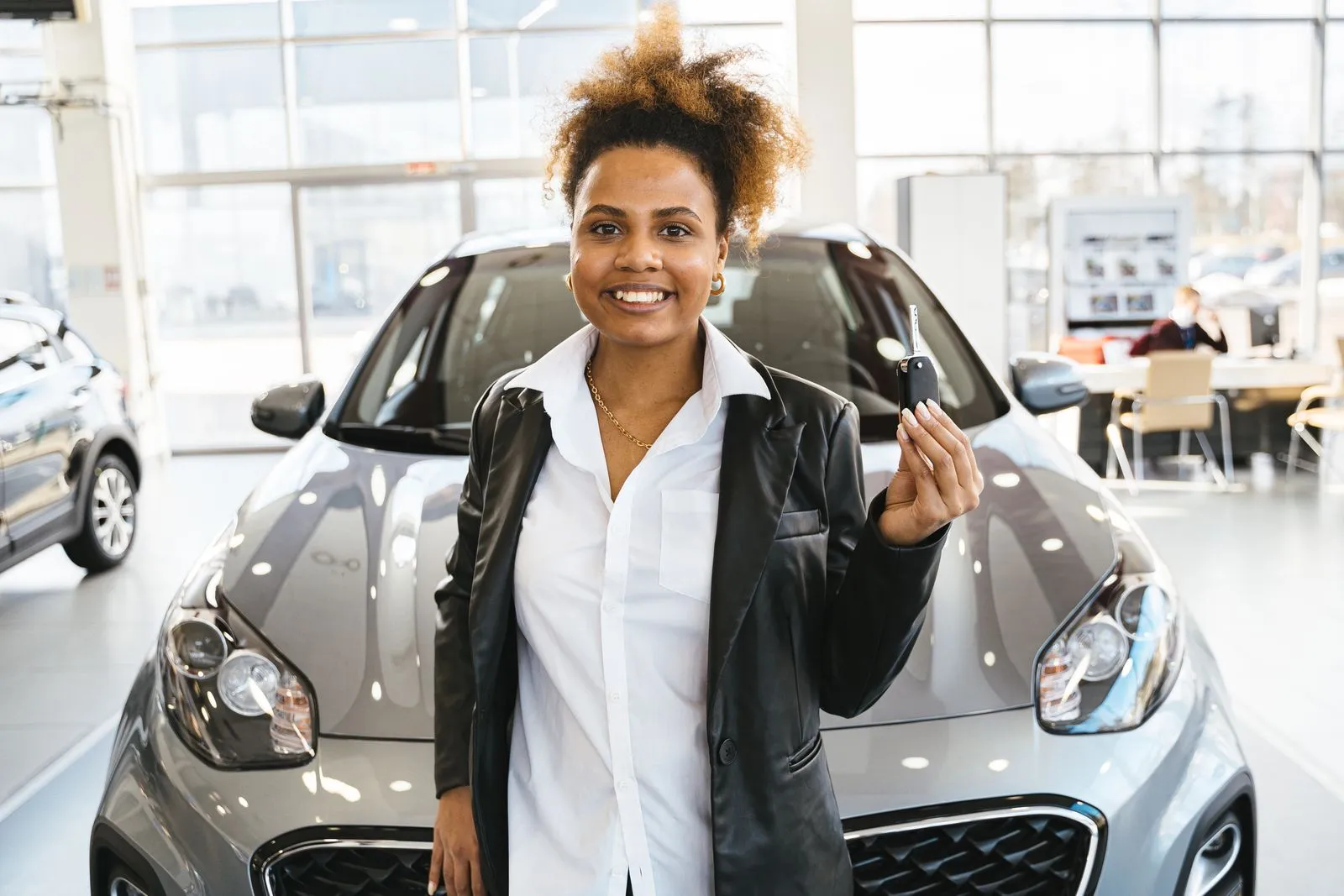 Mulher sorri e mostra a chave do carro que acabou de comprar, na frente do veículo
